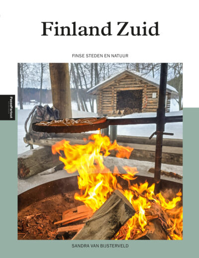 Brandend vuur in een vuurschaal met eten erboven; met op de achtergrond een houten blokhut in een besneeuwd bos