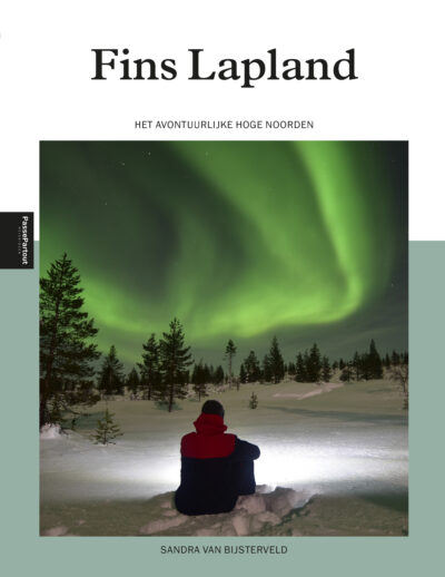 Fins Lapland, reisgids cover. Op de coverfoto een man zittend in de sneeuw, uitkijkend op het noorderlicht.